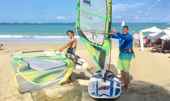 Two people on a beach with windsurf boards, preparing for a thrilling ride.