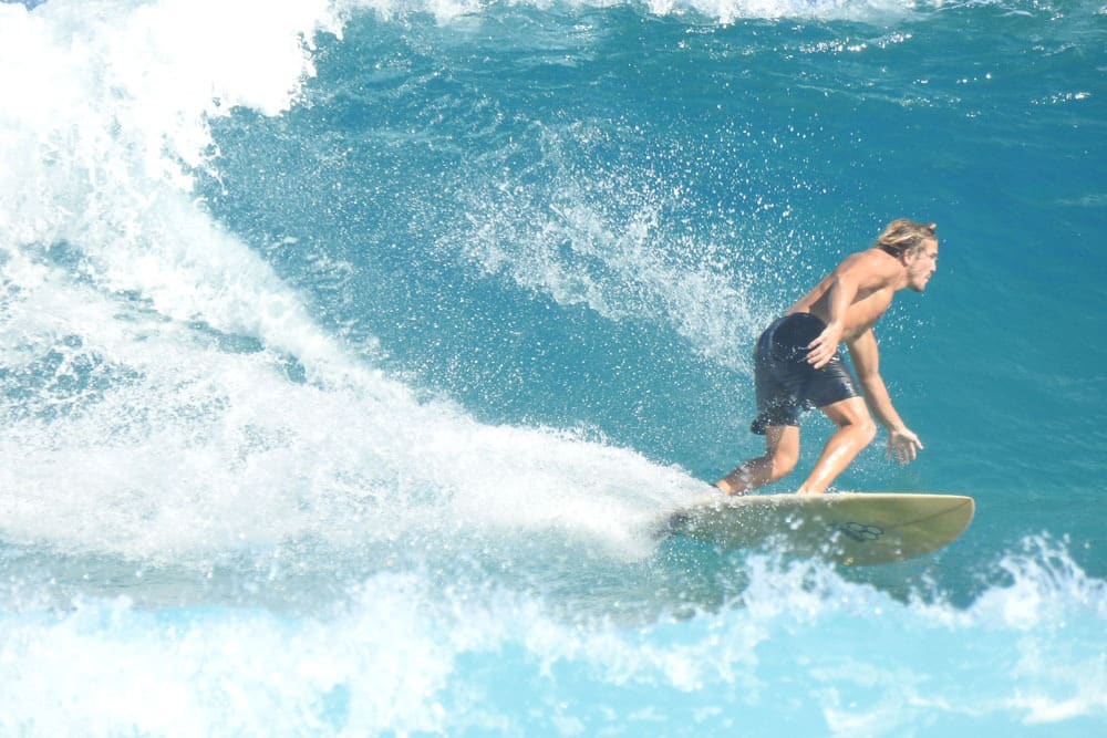Coco Pipe skillfully rides a wave on a surfboard, displaying balance and control amidst the crashing water.