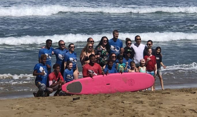 A group of people smiling and posing for a photo with a pink surfboard on a sunny beach of Encuentro, Caberete