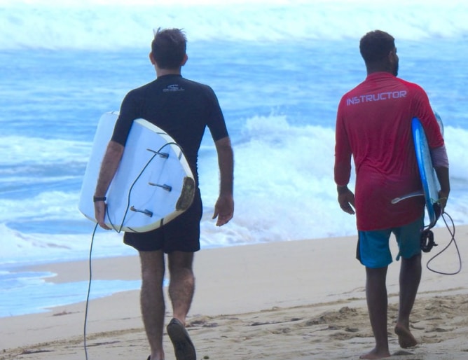 Two men walking on a beach with surfboards, enjoying a sunny day by the ocean.