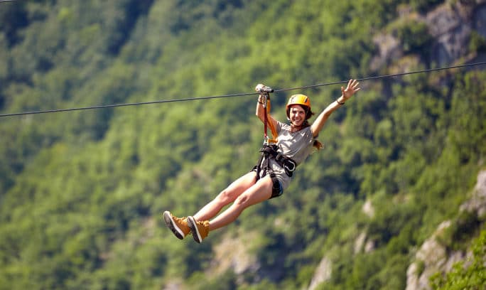A woman soaring on a zipline amidst picturesque mountains, experiencing an exhilarating adventure.